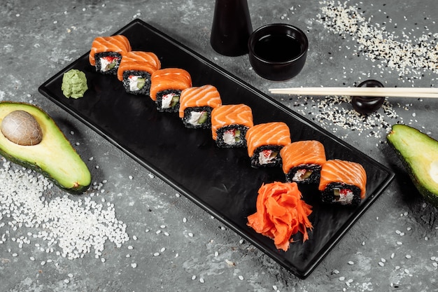 Um conjunto de rolos de sushi da filadélfia com peixe vermelho, cream cheese e ascensão preta encontra-se em um barco de placa. rolos de sushi em um fundo cinza.