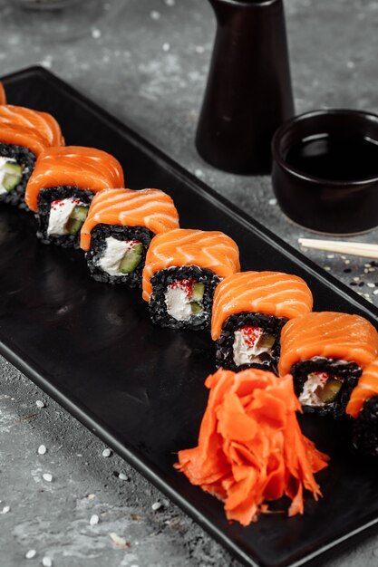 Um conjunto de rolos de sushi da filadélfia com peixe vermelho, cream cheese e ascensão preta encontra-se em um barco de placa. rolos de sushi em um fundo cinza.