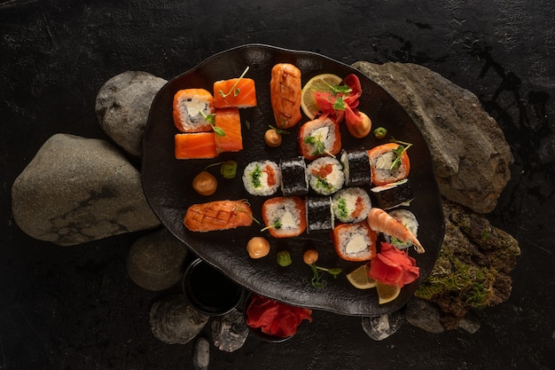 Um conjunto de sushi em uma bela placa preta. Prato japonês de sashimi, pãezinhos, maki, gengibre, wasabi e molho de amendoim