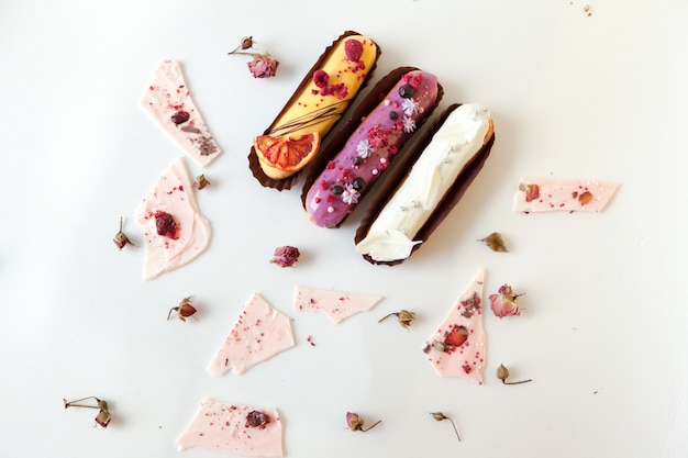 Um conjunto de três eclairs com diferentes recheios e um design isolado em uma superfície branca decorado com rosas secas e pedaços de chocolate brancos