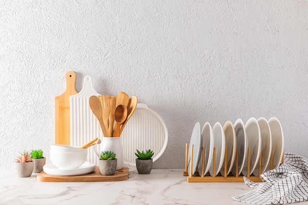 Um conjunto de utensílios de cozinha e pratos em cores claras em uma bancada de mármore branco contra o fundo de um fundo interior de parede texturizada cinza