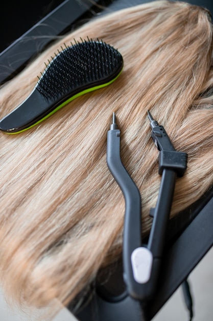 Um conjunto de várias ferramentas de extensão de cabelo para uma mulher loira em um salão de beleza Alicates e micro tubos