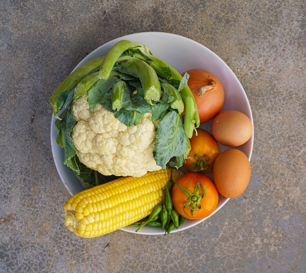 Um conjunto de vegetais crus consiste em couve-flor, cebola, tomate e 2 ovos em um prato