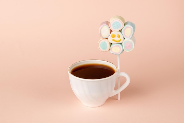 Um conjunto sorridente de marshmallows no palito e uma xícara de café em um fundo bege. O conceito de um café da manhã divertido. Manhã feliz.