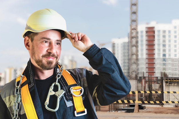 Um construtor masculino em um capacete branco contra um fundo desfocado de um canteiro de obras com um céu azul Engenheiro civil positivo com barba