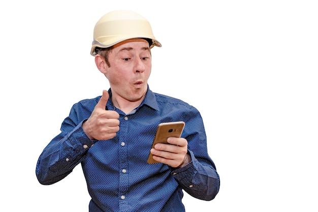 Um construtor ou arquiteto com um capacete em um fundo branco e isolado olha para a tela de um telefone móvel.