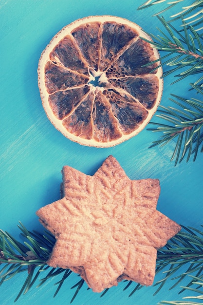 Um cookie em forma de flocos de neve e laranjas secas sobre um fundo azul de madeira