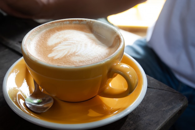 Um copo amarelo de café com leite quente na mesa de madeira