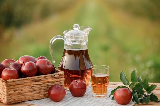 Um copo com suco de maçã e cesta com maçãs na mesa de madeira com fundo natural do pomar Composição de frutas vegetarianas