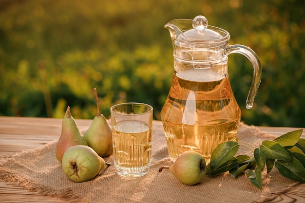 Um copo com suco de pêra e cesta com peras na mesa de madeira com fundo de pomar natural na luz do sol. Composição de frutas vegetarianas