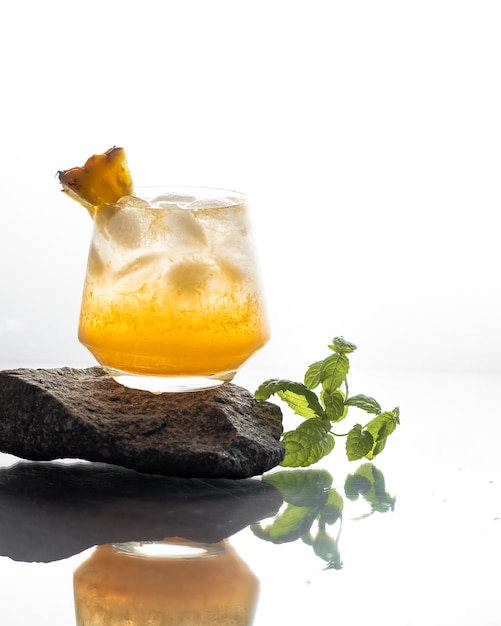 Um copo com um coquetel de rum branco e abacaxi fica em uma pedra cinza sobre fundo branco