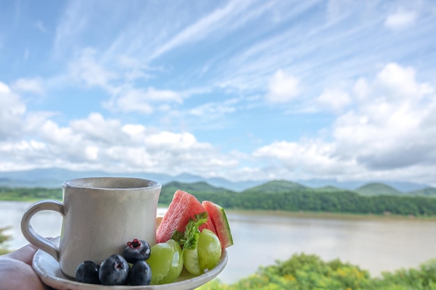 Um copo de água e uma tigela de frutas estão em uma bandeja em frente a uma janela com vista para as montanhas.