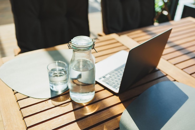 Um copo de água no fundo de um laptop em um terraço de verão Trabalhar em um café Trabalho remoto on-line