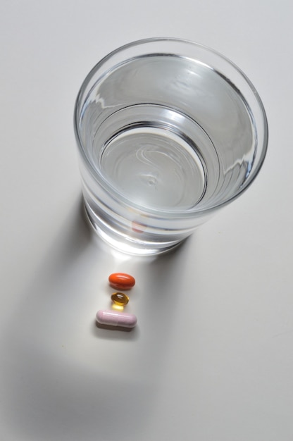 Foto um copo de água potável e várias cápsulas com vitaminas. fundo claro. fechar-se.