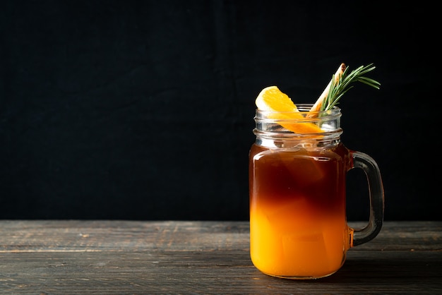 Um copo de café preto americano gelado e uma camada de suco de laranja e limão decorado com alecrim e canela