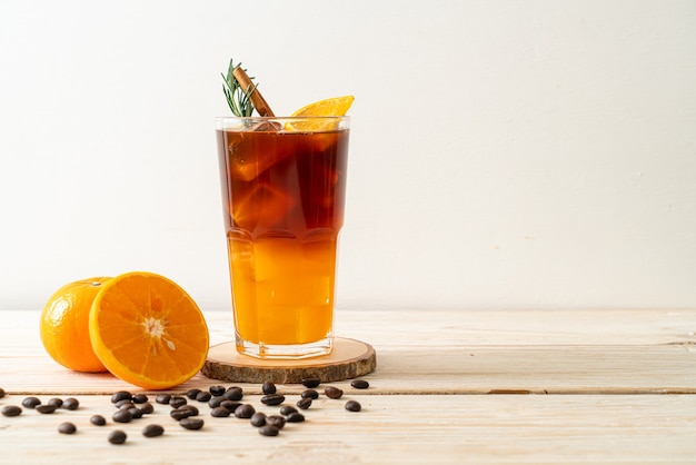 Um copo de café preto americano gelado e uma camada de suco de laranja e limão decorado com alecrim e canela