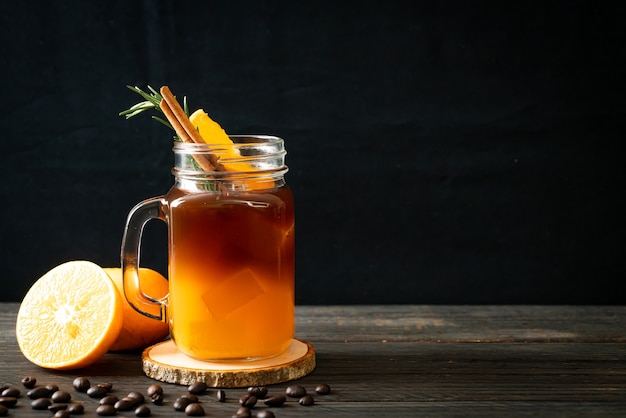 Um copo de café preto americano gelado e uma camada de suco de laranja e limão decorado com alecrim e canela