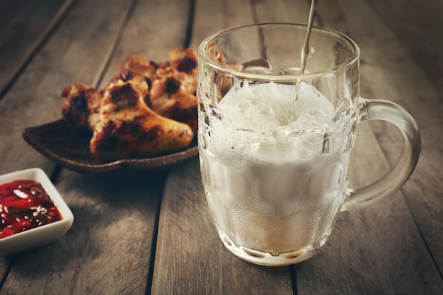 Um copo de cerveja e asas de frango em uma mesa de madeira de perto