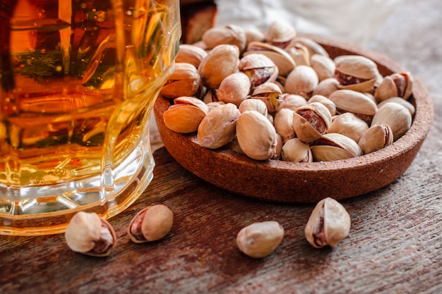 Um copo de cerveja e pistácios salgados em uma mesa de madeira