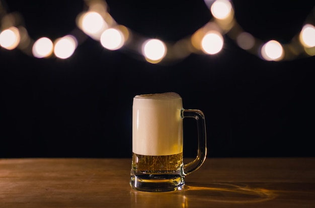 Foto um copo de cerveja em uma mesa de madeira que tem luzes bokeh em cima com fundo escuro