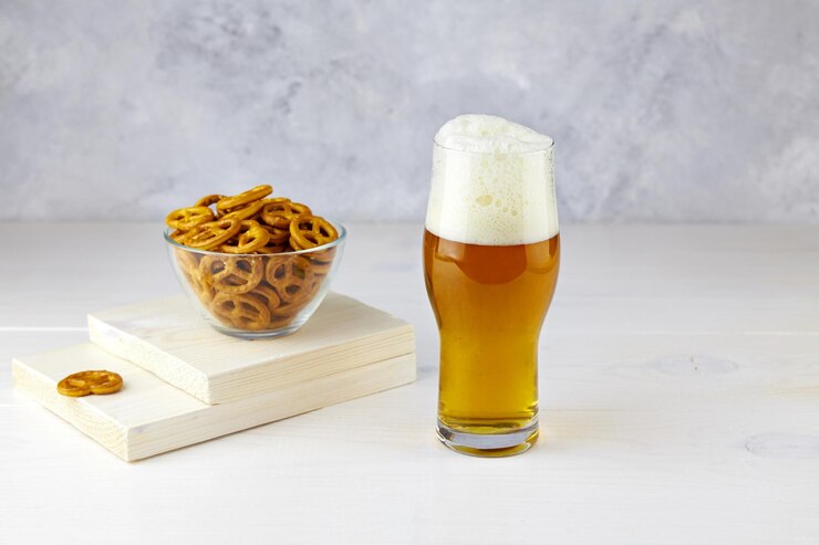 Foto um copo de cerveja leve com pretzels em um fundo de madeira branca