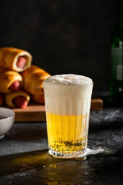 Um copo de cerveja light com espuma e salsichas na massa na tábua de madeira