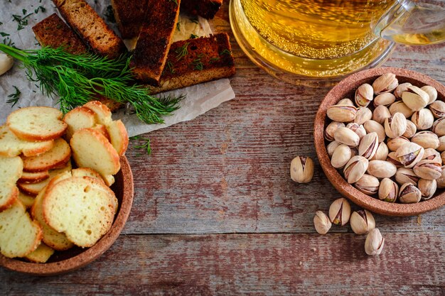 Um copo de cerveja light e lanches, pistache e croutons em uma mesa de madeira