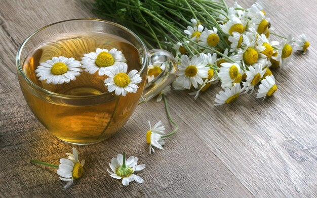 Um copo de chá com margaridas e um vaso de margaridas.