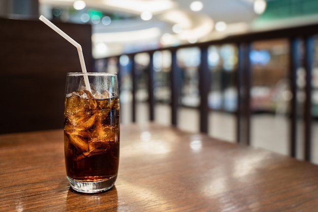 Um copo de coca-cola com cubo de gelo na mesa de madeira sobre o fundo do restaurante turva