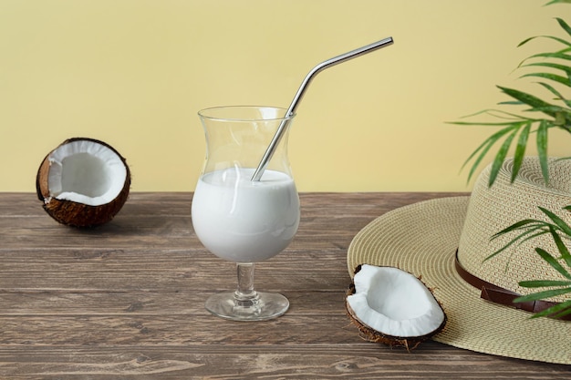 Um copo de coquetel de leite de coco pedaços de coco e um chapéu de verão na mesa de madeira