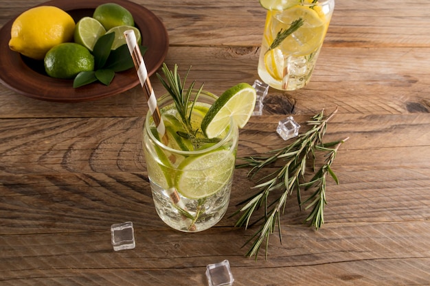 Um copo de cubos de gelo de água de limão e alecrim uma bebida refrescante de verão fundo marrom de madeira com frutas e cubos de gelo