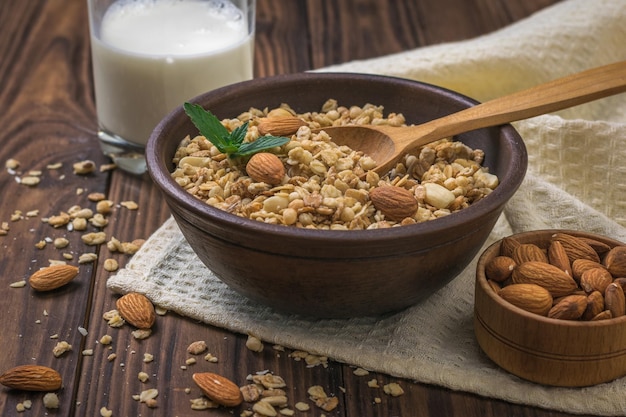 Um copo de granola de leite e uma tigela de amêndoas em uma mesa de madeira