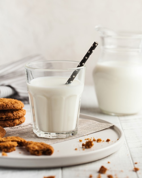 Um copo de leite, biscoitos, uma jarra de leite em uma superfície clara