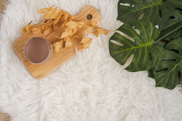 Foto um copo de leite com chocolate quente na placa de madeira, colocado no tapete de pele macia branca pronto para um bom dia no inverno