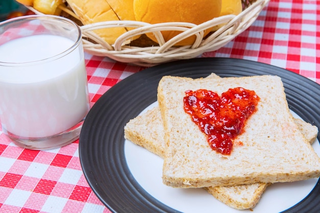 Um copo de leite com pão e geleia de morango.