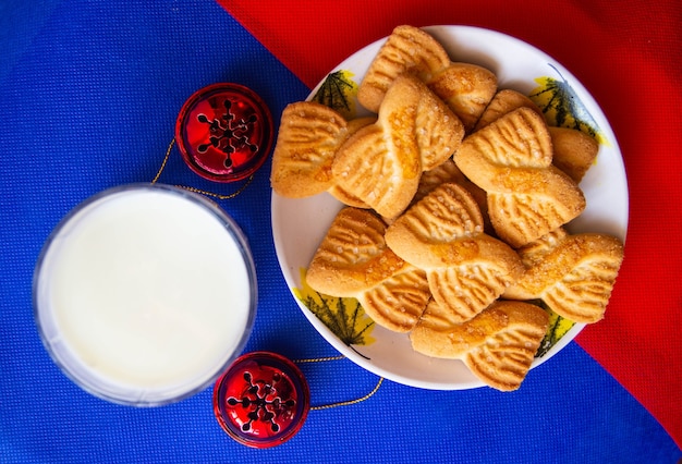 Um copo de leite e biscoitos ou biscoitos no prato com sinos vermelhos. fundo do dia nacional do biscoito. café da manhã de natal para o papai noel. café da manhã americano