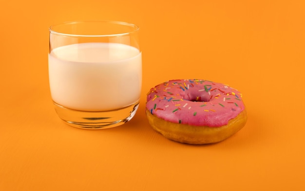 Um copo de leite e uma rosquinha rosa em um fundo laranja.