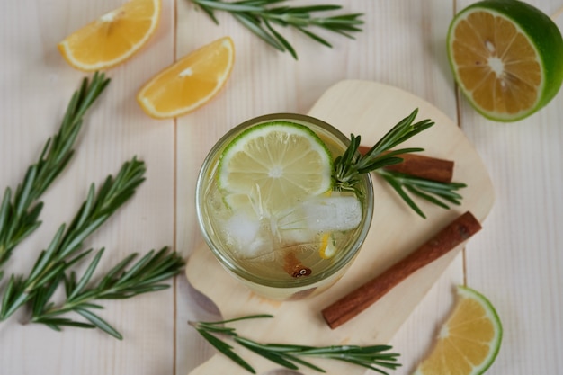 Um copo de limonada com limão fresco e lima, decorado com um galho de alecrim em um fundo claro de madeira, vista de cima