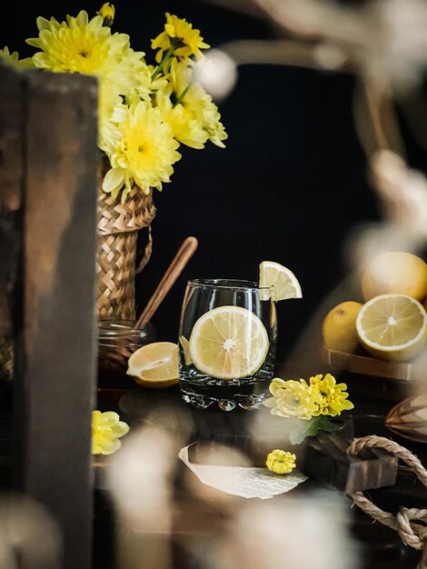 Um copo de limonada está sobre uma mesa com flores ao fundo.