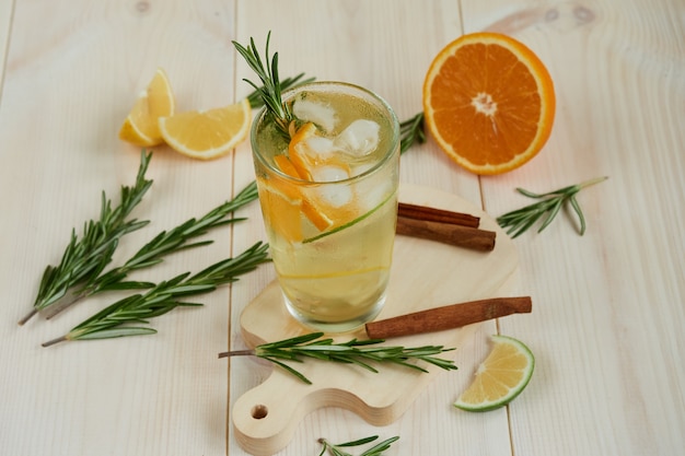 Um copo de limonada gelada com frutas cítricas e alecrim e canela em uma mesa de madeira