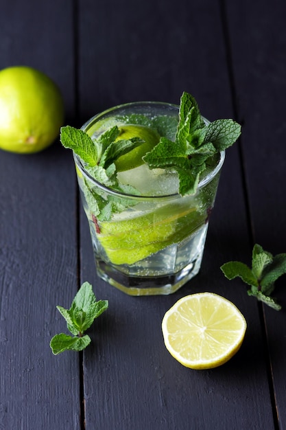 Um copo de mojito frio com limão limão e hortelã em um fundo preto de madeira Fechamento de um coquetel refrescante