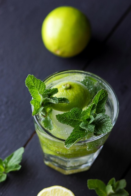 Um copo de mojito frio com limão limão e hortelã em um fundo preto de madeira Fechamento de um coquetel refrescante