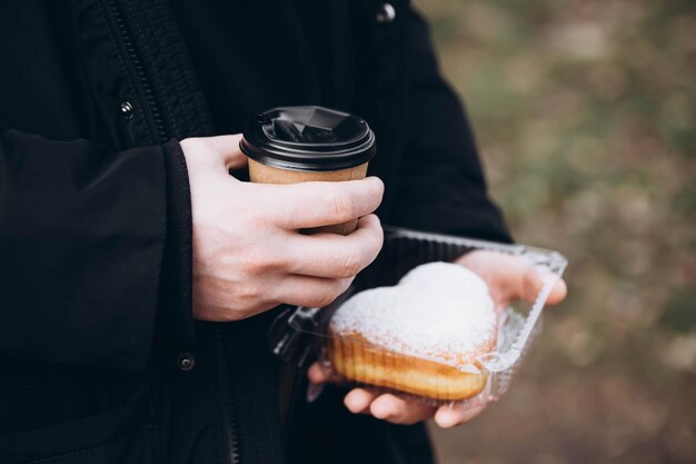 Um copo de papel de café e um donut em forma de coração em mãos masculinas em close-up