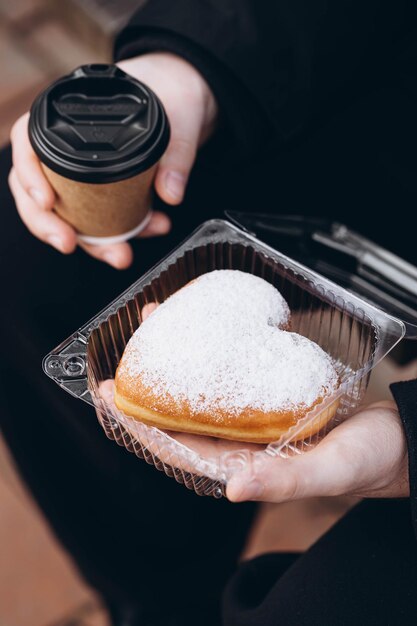 Um copo de papel de café e um donut em forma de coração em mãos masculinas em close-up