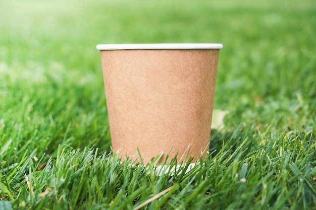 Um copo de papel em um fundo de grama. Copo marrom para bebidas.