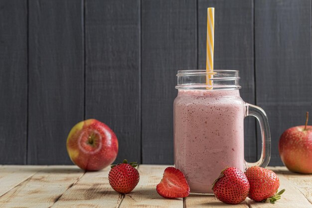 Um copo de purê de milk-shake de morango fresco e morangos frescos em um fundo de madeira