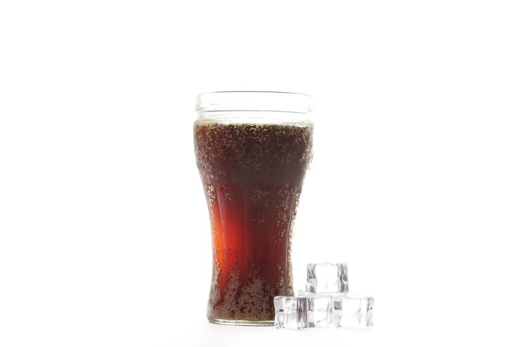 Foto um copo de refrigerante marrom escuro ao lado de dois cubos de gelo.