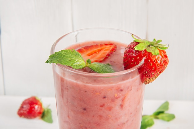 Um copo de smoothie de morango e banana saudável em fundo branco de madeira decorado com hortelã. Fechar-se