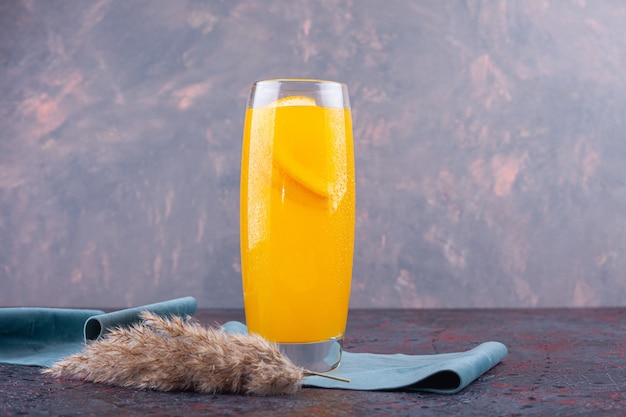 Um copo de suco de laranja com uma fatia de fruta colocado em um colorido.