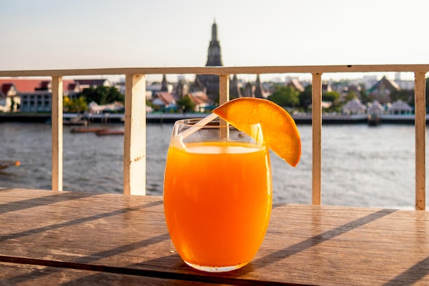 Um copo de suco de laranja está sobre uma mesa em um bar na cobertura com um famoso marco ao fundo. Bangkok, Tailândia